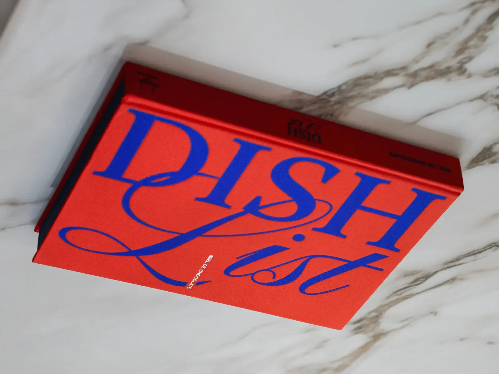 Libro Dish List de tela roja con tipografía azul cobalto sobre mármol blanco.